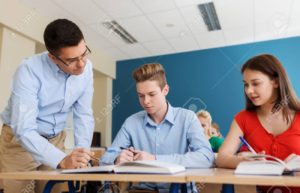 education, school, learning, teaching and people concept - group of students and teacher talking in classroom